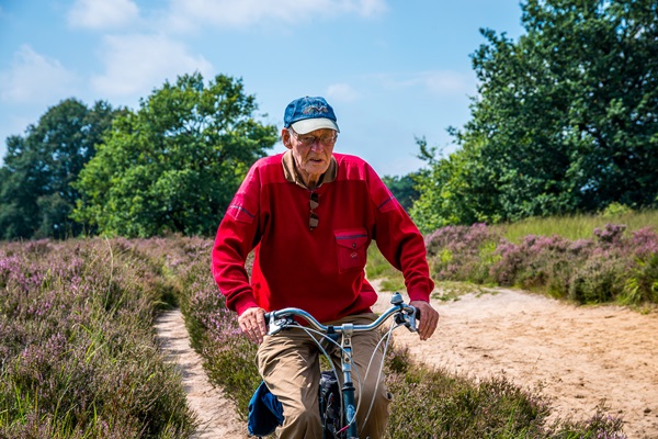 Oudere man fiets over een zandpad door Nationaal Park De Meinweg
