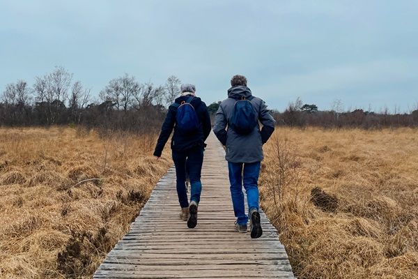 Twee wandelaars op een knuppelbrug in De Groote Peel tijdens een winterwandeling door het veengebied.