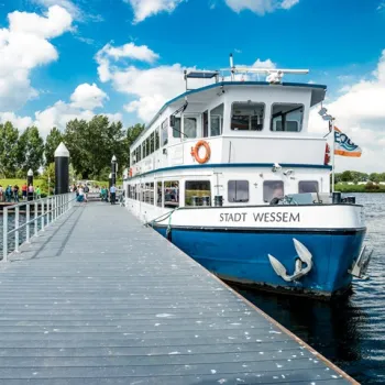 Rondvaartboot Stadt Wessem ligt aangemeerd aan de steiger op de Maasplassen onder een blauwe lucht.