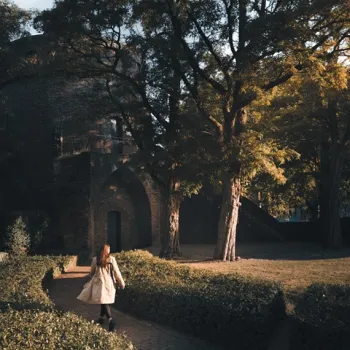 Vrouw wandelt in haar eentje door een sfeervol park met herfstkleuren, langs een historisch gebouw in Limburg.