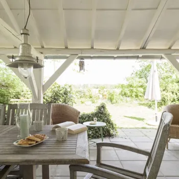 Vakantiehuis met overdekt terras, houten meubels en uitzicht op de landelijke tuin.