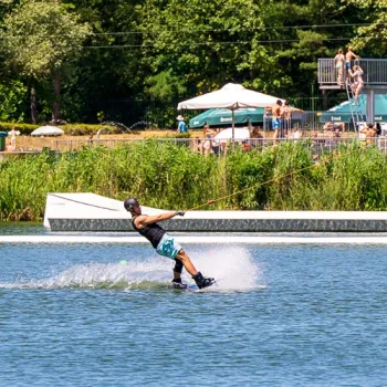 Wakeboarder op de waterskibaan De IJzeren Man in Weert, met terras en recreanten op de achtergrond.