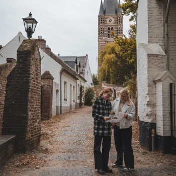 Twee personen bekijken een kaart in een smalle straat in Thorn, met witte huizen en de kerk op de achtergrond.